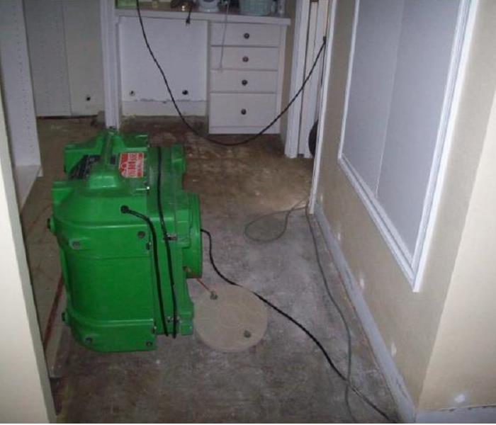 A green dehumidifier drying grey bare floors. 
