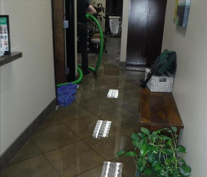 An office with visible water throughout the hallway and a technician extracting in the background.