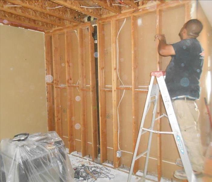 A technician inspecting a bare wall with clean studs that has been cleaned from fire damage.