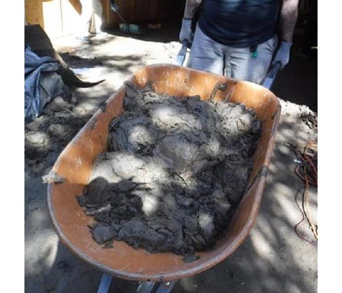Mud being carried in an orange wheel barrow out of a garage.