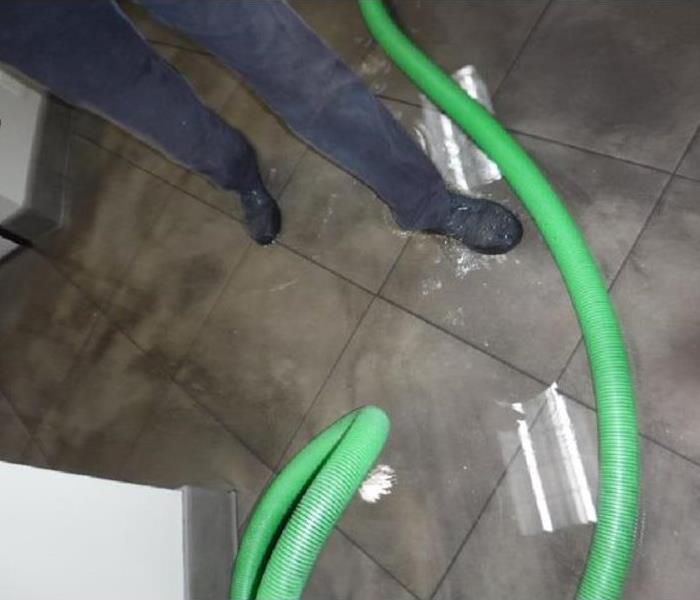A water technician's feet walking through a flooded office with a visible SERVPRO green hose to extract.