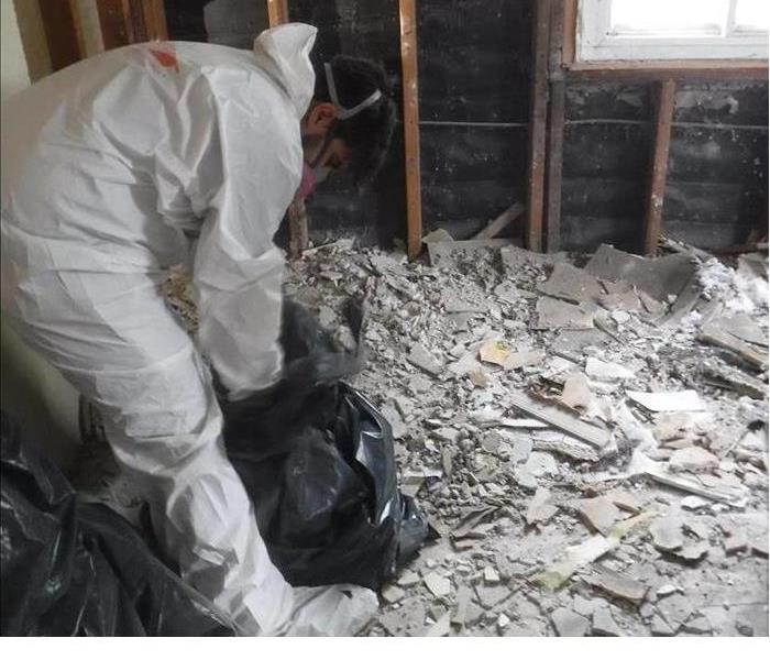 A technician dressed in a PPE suit cleaning up demoltion.